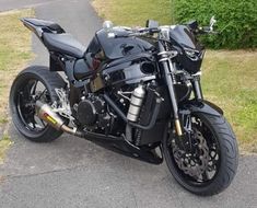 a black motorcycle parked on the side of a road next to grass and bushes in front of a house