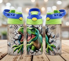 three children's sippy cups with dinosaurs on them sitting on a wooden table