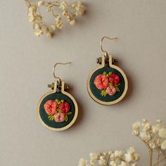 two embroidered earrings with flowers on them sitting next to some dried flowers and white flowers