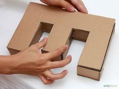 two hands are holding a cardboard letter h