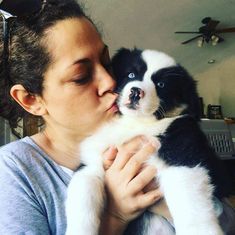 a woman holding a puppy in her arms and kissing it's face with blue eyes