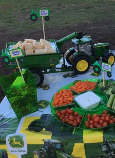 a table topped with green trays filled with vegetables next to tractors and other farm equipment