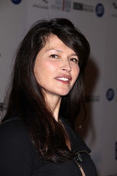 a woman standing in front of a white wall and looking at the camera with a smile on her face