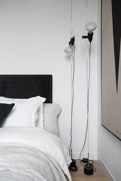 a white bed with two black and white lamps on the headboard next to it