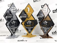 three trophies with numbers on them sitting in front of a white wall and black and yellow background