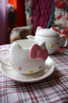 two hello kitty tea cups and saucers sitting on a plaid tablecloth covered table