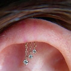 a close up view of a person's ear with three tiny diamond earrings hanging from it