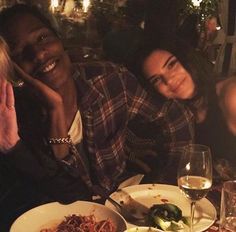 three people sitting at a table with plates of food and wine in front of them