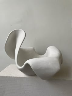 a white sculpture sitting on top of a block of concrete in front of a wall