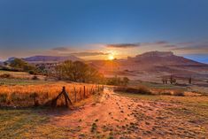 the sun is setting over an open field with mountains in the backgrouds