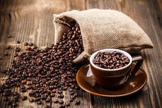 coffee beans spilling out of a bag next to a cup and saucer on a wooden table