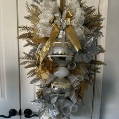 a christmas wreath with silver and gold decorations hanging from the front door, on a white door