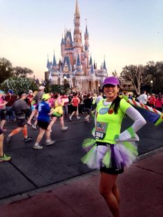 a woman standing in front of a castle at the disney world marathon with her arms behind her back