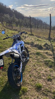 a blue and white motorcycle parked on top of a grass covered field next to a fence