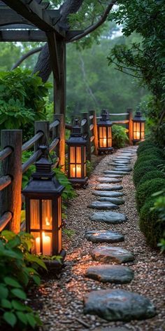 lanterns lit up in the middle of a path surrounded by trees and bushes with rocks on either side