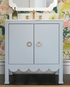 a bathroom vanity with two gold handles and a mirror above it, against a floral wallpaper