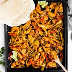 chicken fajita and tortillas on a black tray with lime wedges