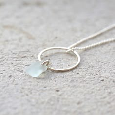 a small white sea glass necklace on a silver plated chain, sitting on the sand