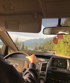 a person driving a car on a road with mountains in the background