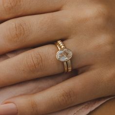 a woman's hand wearing a gold ring with an oval shaped diamond on it