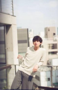 a young man standing on top of a balcony next to a tall building with buildings in the background