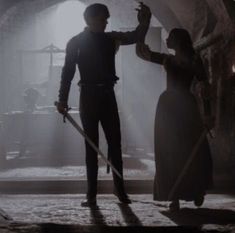 a man and woman holding swords in a dark room