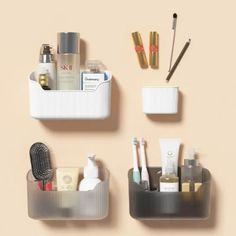 three plastic containers with various items in them on a beige surface, one containing toothbrushes and the other containing cosmetics