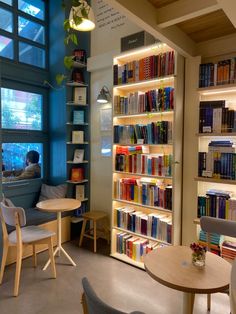 a library filled with lots of books next to a table and chairs in front of a window