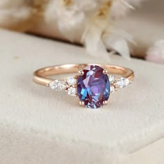 an oval shaped purple and white sapphire ring with three diamonds on the band, set in 18k rose gold