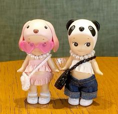 two little dolls are standing on a wooden table with one holding the other's hand