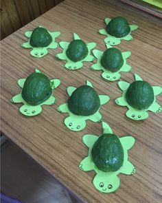 there are many little turtles made out of green paper on the wooden table with books in the background