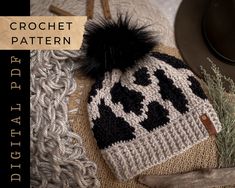 a crochet hat with a black and white pattern on it, next to a plant