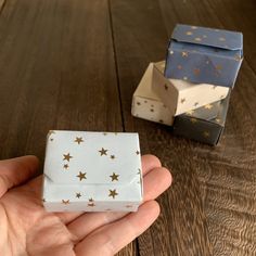 a hand holding a small gift box with gold stars on it next to another one