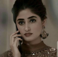 a woman talking on a cell phone while wearing gold jewelry and holding her hand up to her ear