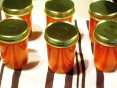 six orange jars with green lids sitting on a striped table cloth next to each other