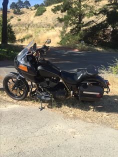 a black motorcycle parked on the side of a road next to a tree filled hill