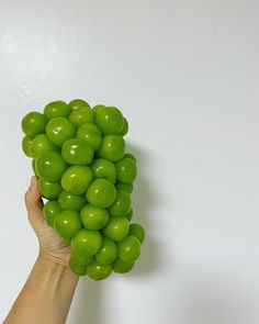 a hand holding a bunch of green grapes on top of a white wall in front of a person's hand