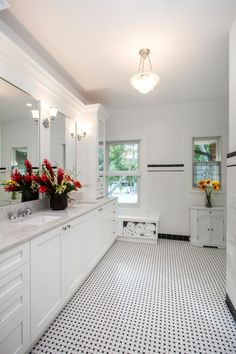 a white bathroom with black and white flooring and flowers in vases on the sink