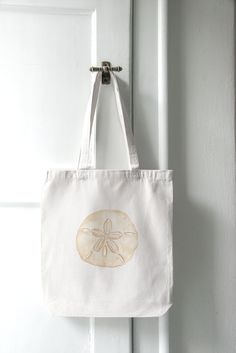 This coastal canvas tote bag is ready for a trip to the beach. Whether you're heading to the beach, strolling through a farmer's market, or simply running errands around town, this tote bag is your ideal companion. This Sand Dollar Cotton Canvas Tote Bag is the perfect blend of coastal charm with a trendy tan design.  🐚 Design: The Sand Dollar Tote Bag features a neutral watercolor painting that evokes the calmness of a morning by the beach. Its intricate sand dollar pattern, rendered in soft, earthy tones, adds a touch of coastal allure to your style, making it perfect for beach lovers and ocean enthusiasts. 🌞 Quality: Crafted from high-quality, durable cotton canvas, this tote bag is built to withstand the test of time. Rest assured that you can carry your essentials, from groceries an Eco-friendly White Canvas Bag With Canvas Lining, Eco-friendly White Canvas Bag, White Beach Bag With Canvas Lining, White Beach Bag With Canvas Lining For Everyday, White Everyday Beach Bag With Canvas Lining, Casual White Beach Bag With Canvas Lining, Cotton Beach Tote Bag For Beach Season, Cotton Tote Beach Bag For Beach Season, Beachy Cotton Rectangular Beach Bag