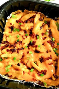 an enchilada dish in a black container with green onions and cheese on top