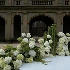 white flowers and greenery are arranged on a table in front of an old building