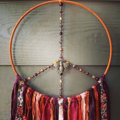 a peace sign made out of beads and tassels hanging from a wooden wall