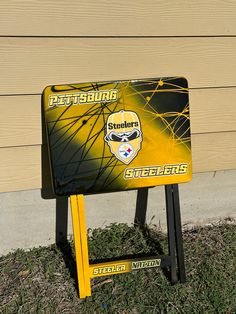 a pittsburgh steele sign sitting in the grass next to a building with a wooden wall behind it