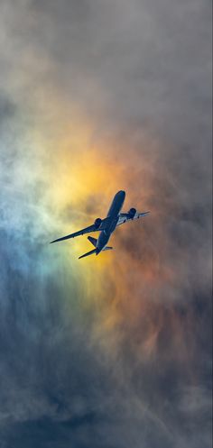 an airplane flying in the sky with a rainbow colored cloud behind it and some clouds