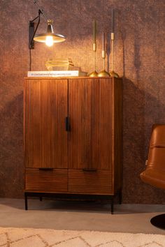 a wooden cabinet sitting next to a brown chair in front of a wall mounted lamp