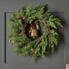 a wreath with bells and pine cones hanging on the wall next to a light switch