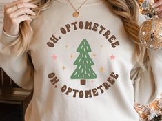 "This comfy pullover is a fun Christmas sweater for an optometry doctor, assistant, tech, and/or staff! \"Oh, optometree\" is featured in a fun, retro font around groovy holiday tree graphic. The sweater is so soft and comfortable for those long nights studying as you earn your optometry degree or in your ophthalmologist office over scrubs. This also makes a great graduation gift for an optometry student, someone already in the field, or for ophthalmologist office staff! Shop more optometry item Optician Marketing, Optometry Student, Doctor Assistant, Optometry Office, Great Graduation Gifts, Dental Student, Office Staff, Gifts For Dentist, Tree Graphic