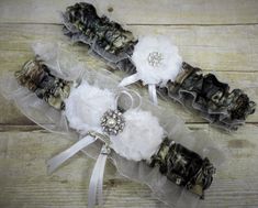 This adorable garter set is made with brown True Timber MC2 Satin Camo print, white organza, with white shabby chic flowers and matching ribbon and are embellished with a pearl and rhinestone brooch. You have the option to have no charm added or choose between different charms to add that personal touch! Included in the set is a beautiful Keepsake garter as well as a Toss-away garter. These garters are made of quality fabric, lace and ribbons. Relaxed these garters measure 15 in. Stretched they Camo Wedding Garters, Mossy Oak Wedding, Camo Prom, Camouflage Wedding, Prom Garters, White Garters, Shabby Chic Flowers, Bridal Garters Set, Camo Wedding