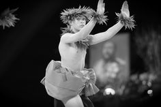 a young boy dressed as a hula dancer with feathers on his head and hands in the air