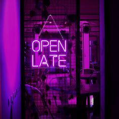 an open late neon sign is lit up in the dark with purple lighting behind it